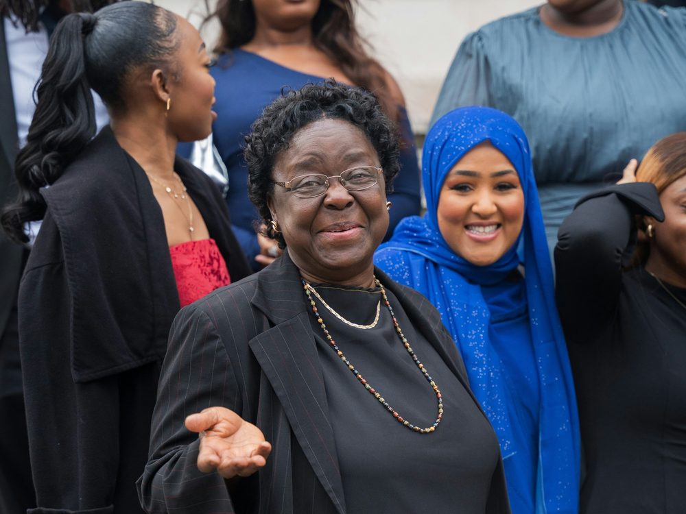 An older woman among a group of younger women, mid-conversation.