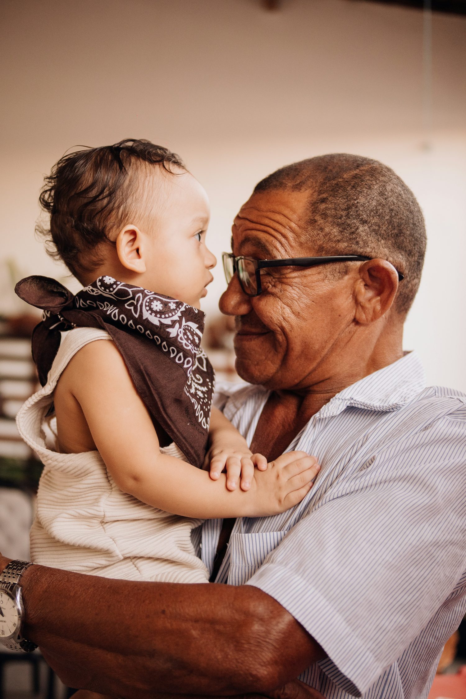 A grandfather holding his grandchild, the two of them looking closely at one another.