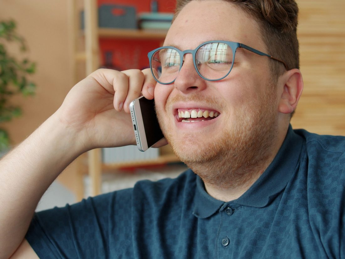 A man laughing with delight, the phone held to his ear, mid-conversation at home.