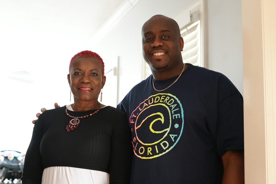 An older woman standing with her adult son, both smiling at the camera.
